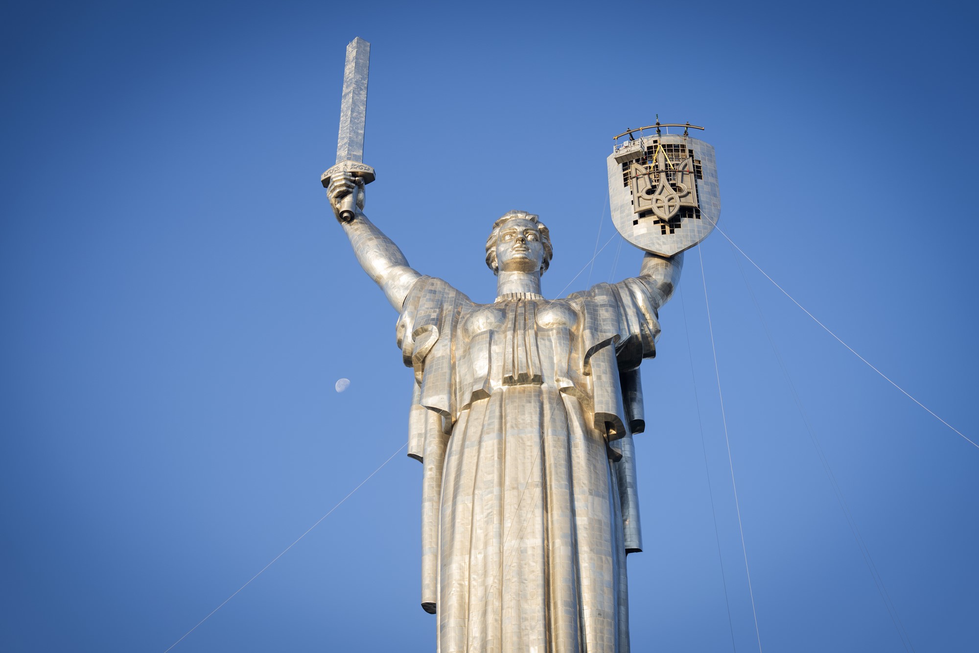 A wide photo looking upwards towards a large outdoor statue of a woman holding a sword and shield