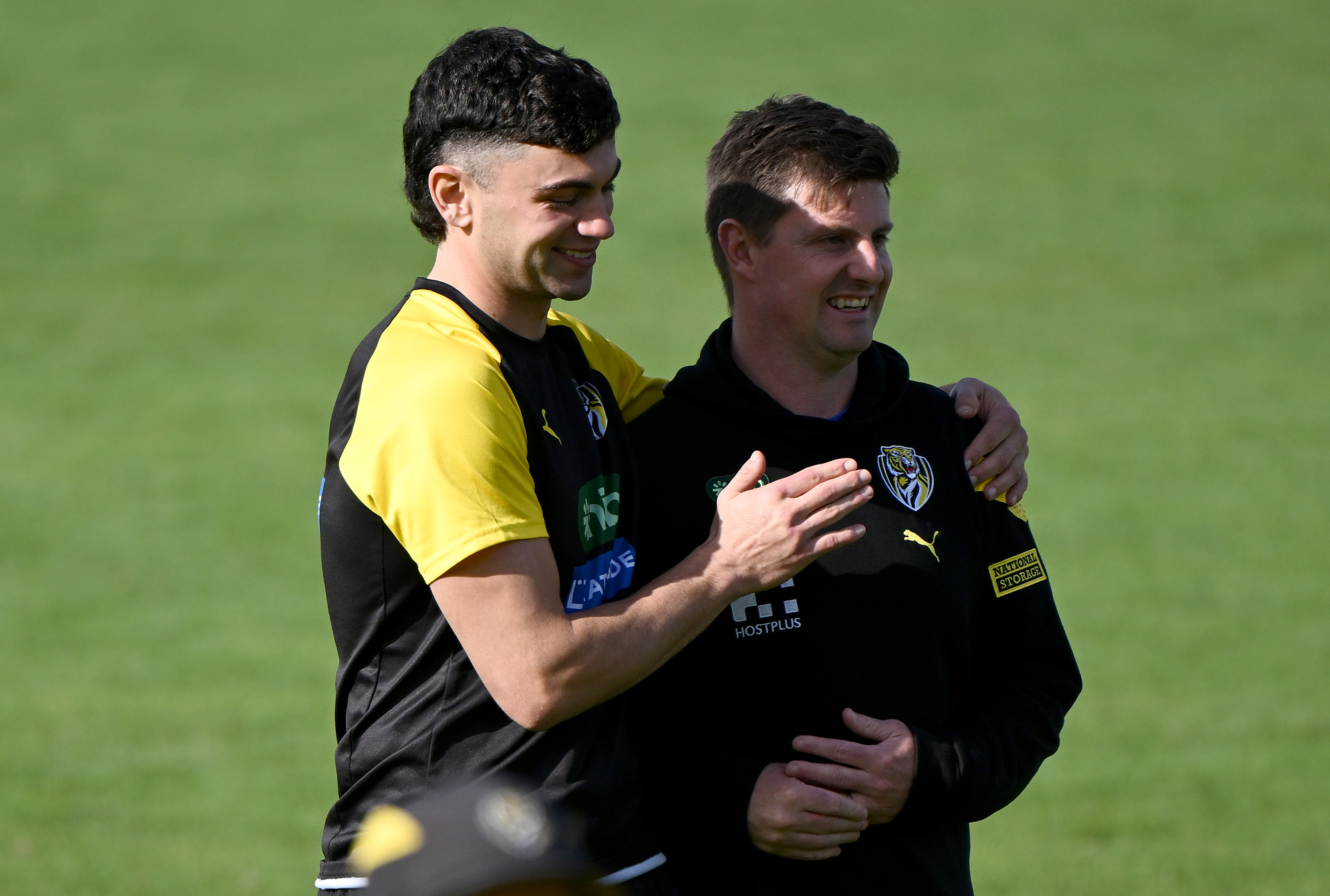 Two man stand next to each other on a field wearing yellow and black.