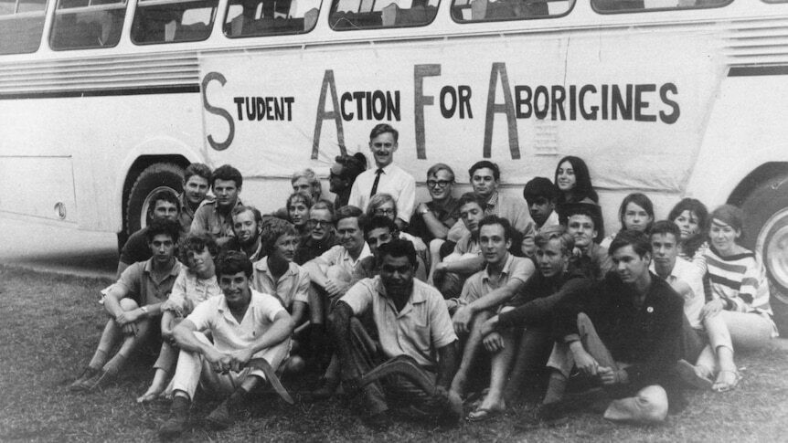 A black and whitep photo from the 60s of students sitting in front of a bus in front of a banner that says Student Action for Aborigines.