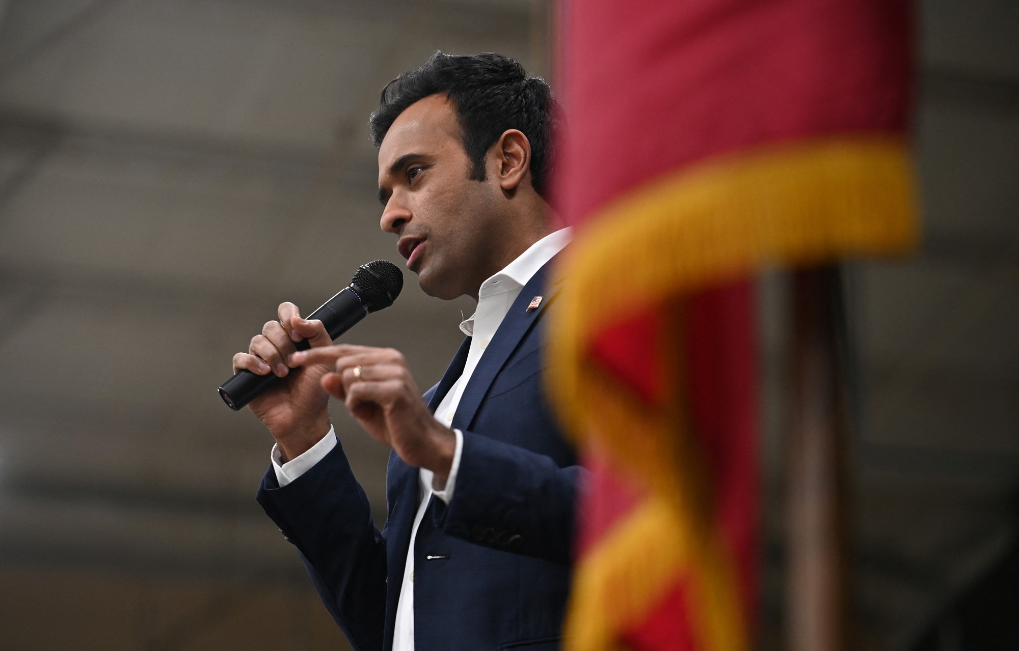 Vivek Ramaswamy speaks into a microphone, from behind a flag pole