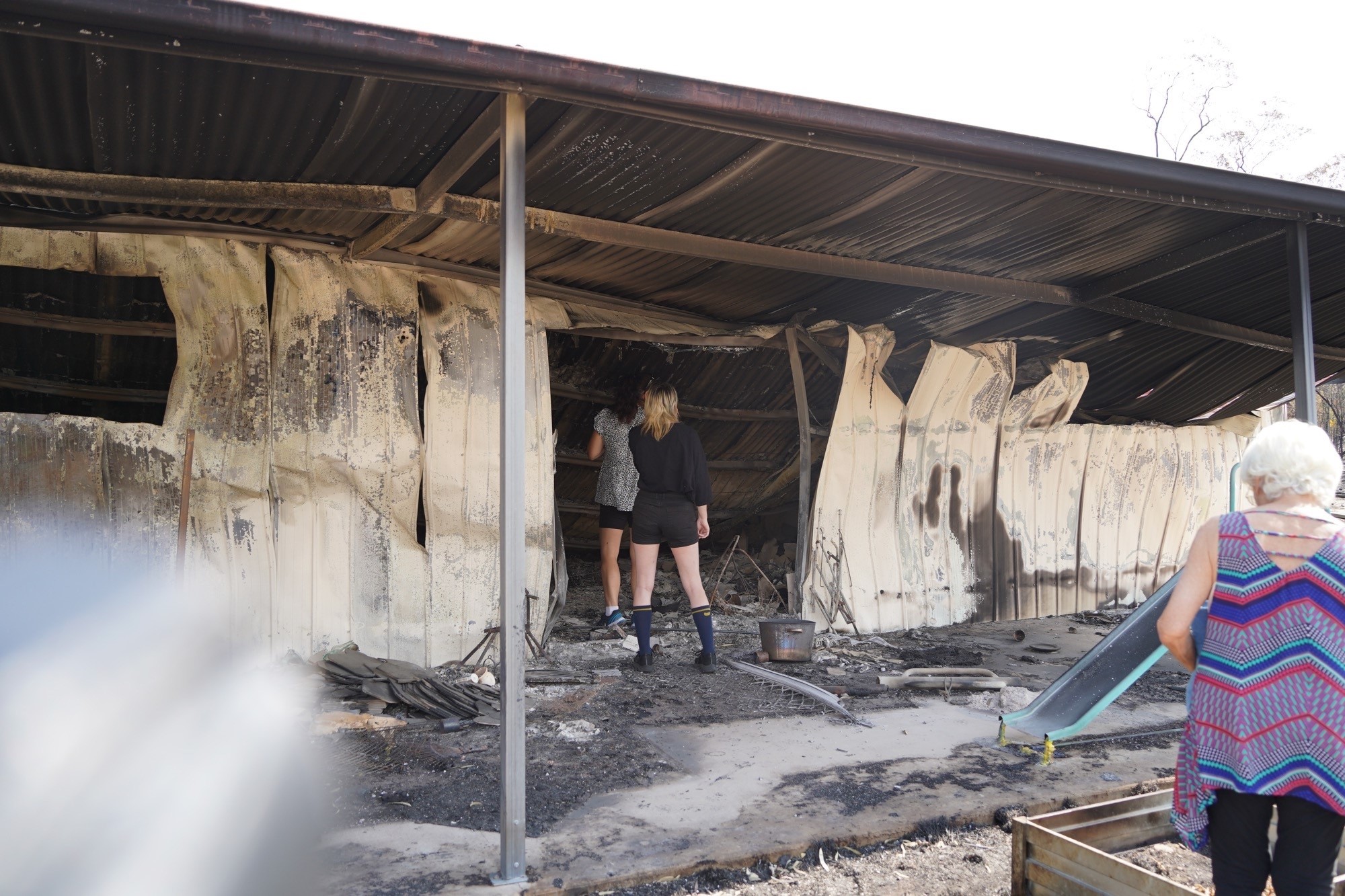 women walk through the wreckage of a burnt-out house