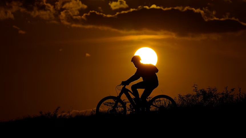 A silouette of a person riding a bike at sunset, with the sun behind them