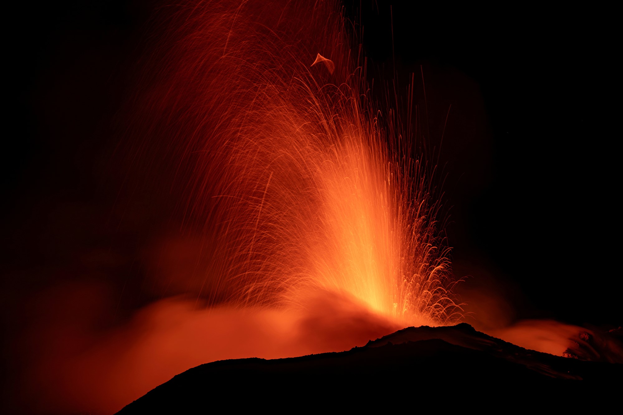 Red light spews from a volcano. 