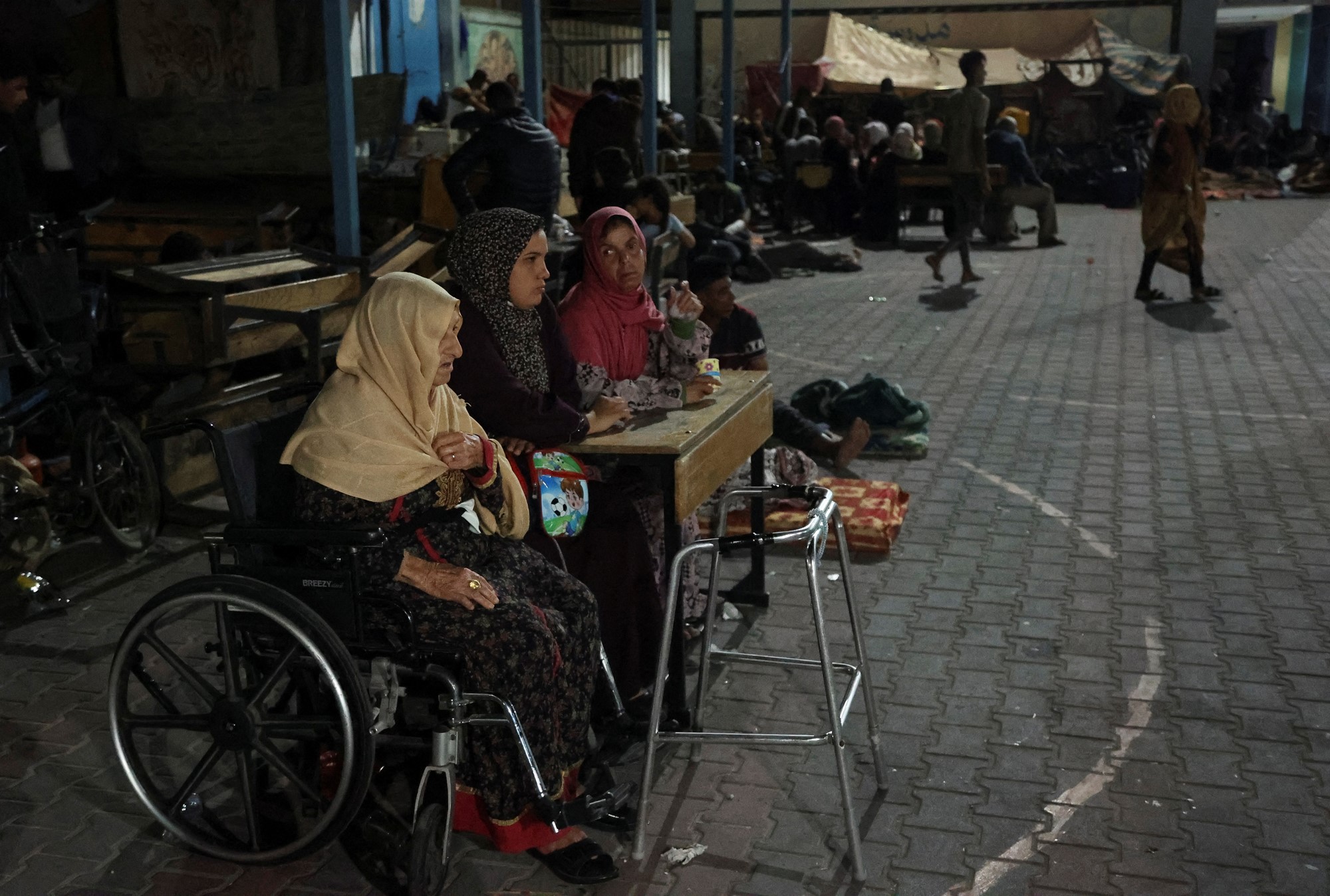 Three women sit around a table in a courtyard, one is in a wheelchair. 