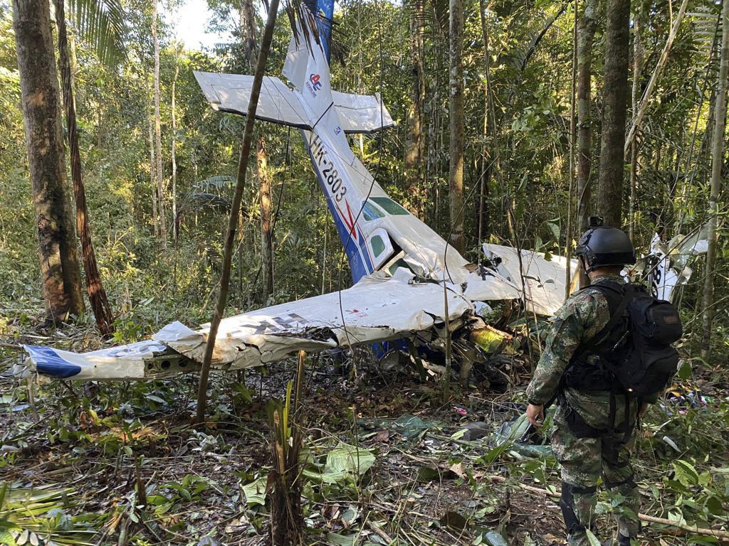 A small plane which has crashed in a dense forest. A man in miltary uniform stands nearby