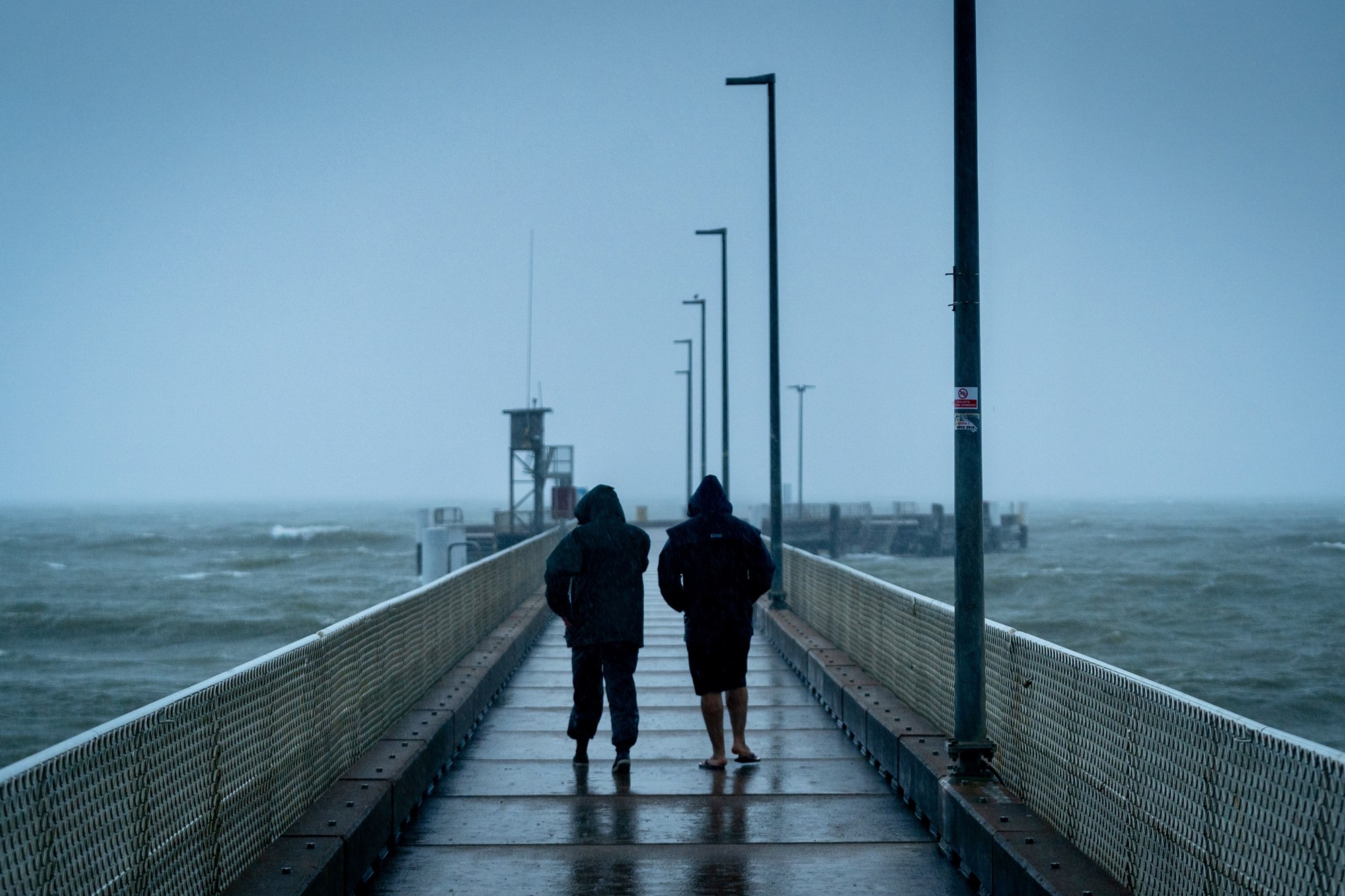 two people walking against wind and rain on a sea jetty
