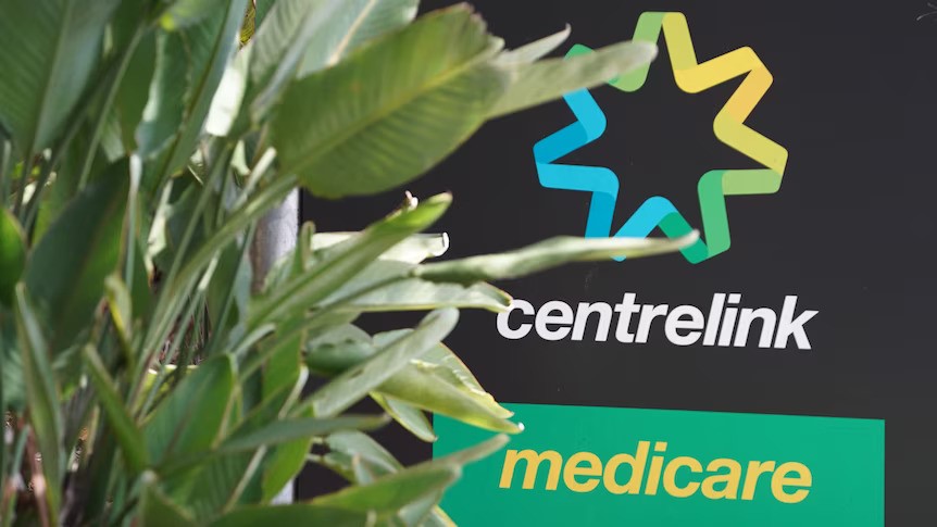 A Centrelink office sign, showing medicare logo, in front of a plant