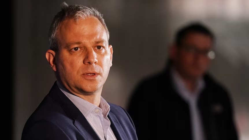 A silver-haired middle-aged man in blue blazer speaks at news conference