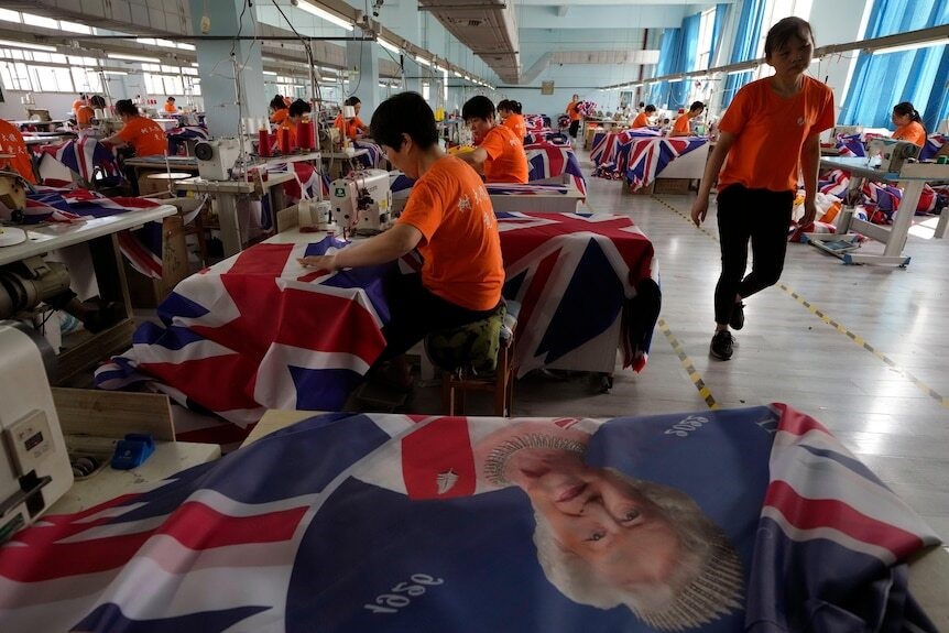 Factory workers sew British flags with the Queen's face on them