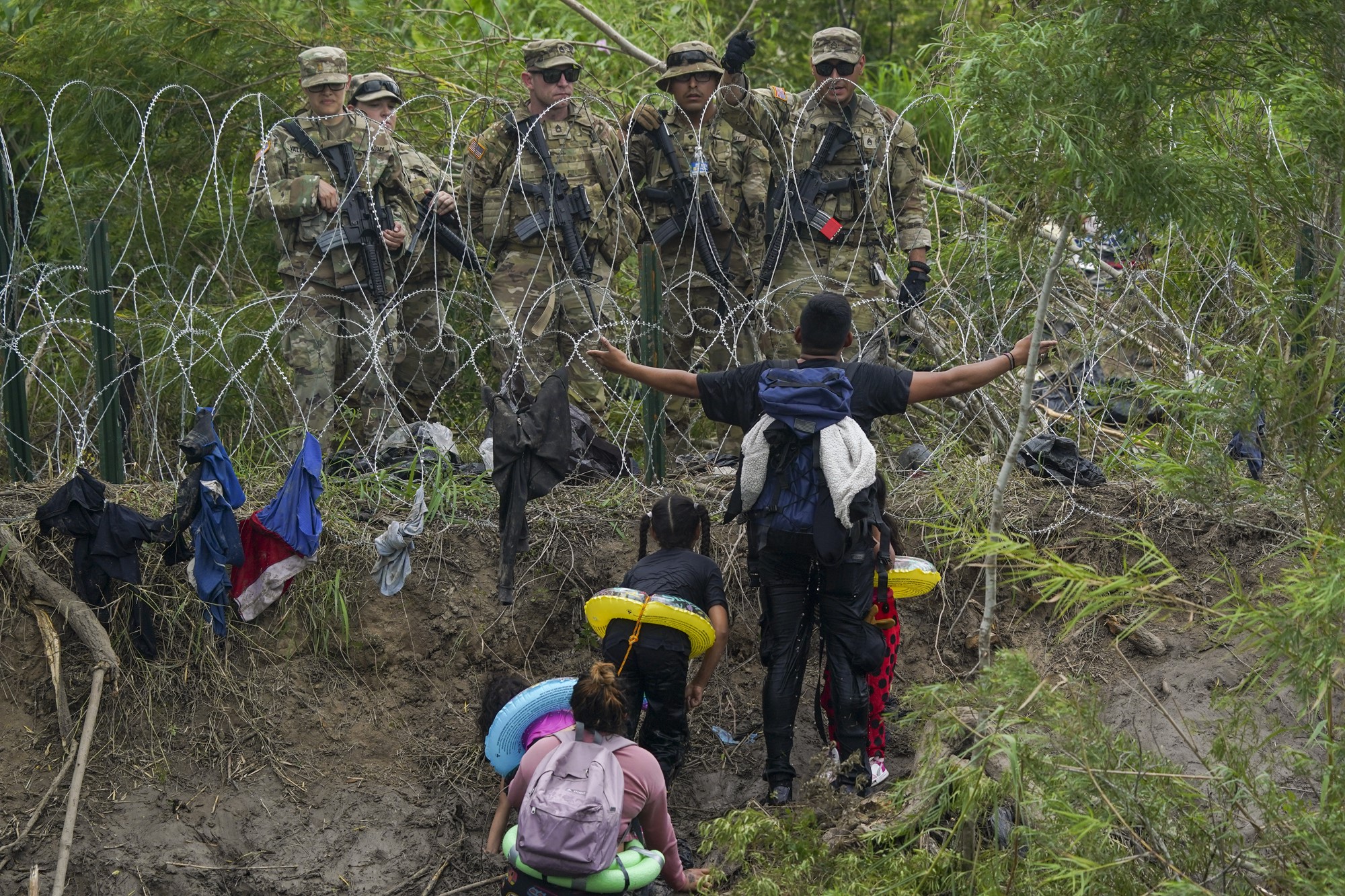 A migrant gestures to Texas National Guards standing behind razor wire on the bank of the Rio Grande river.