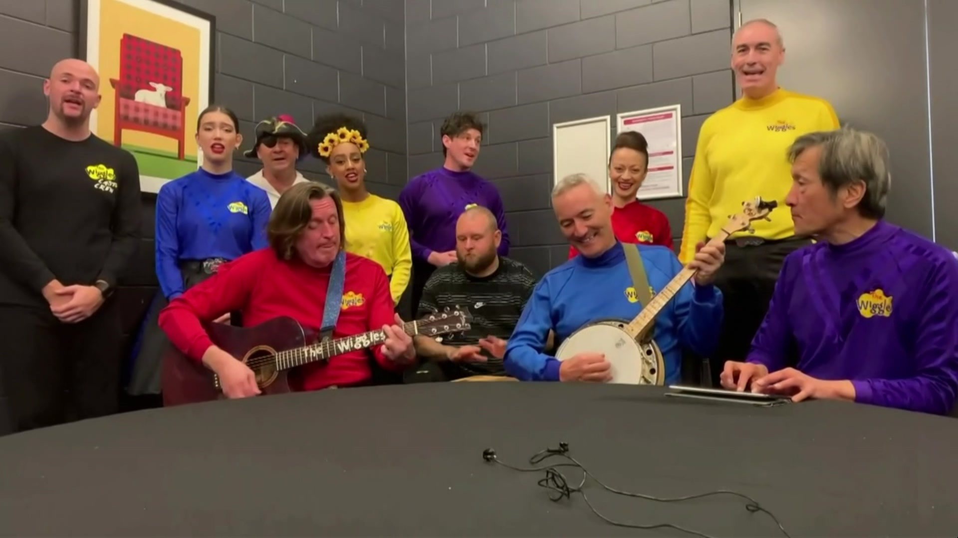 The Wiggles band in colourful skivvies play around a table.