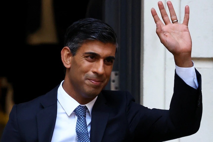 An Indian man wearing a suit waves.