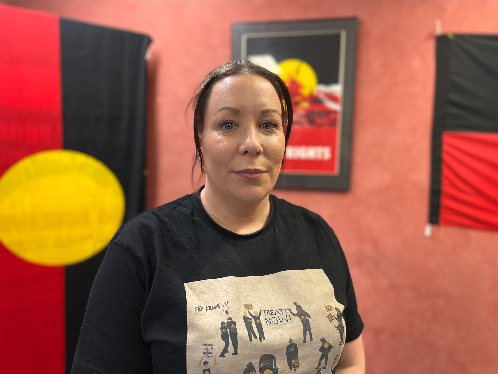 A young Aboriginal woman stands in front of an Aboriginal flag.