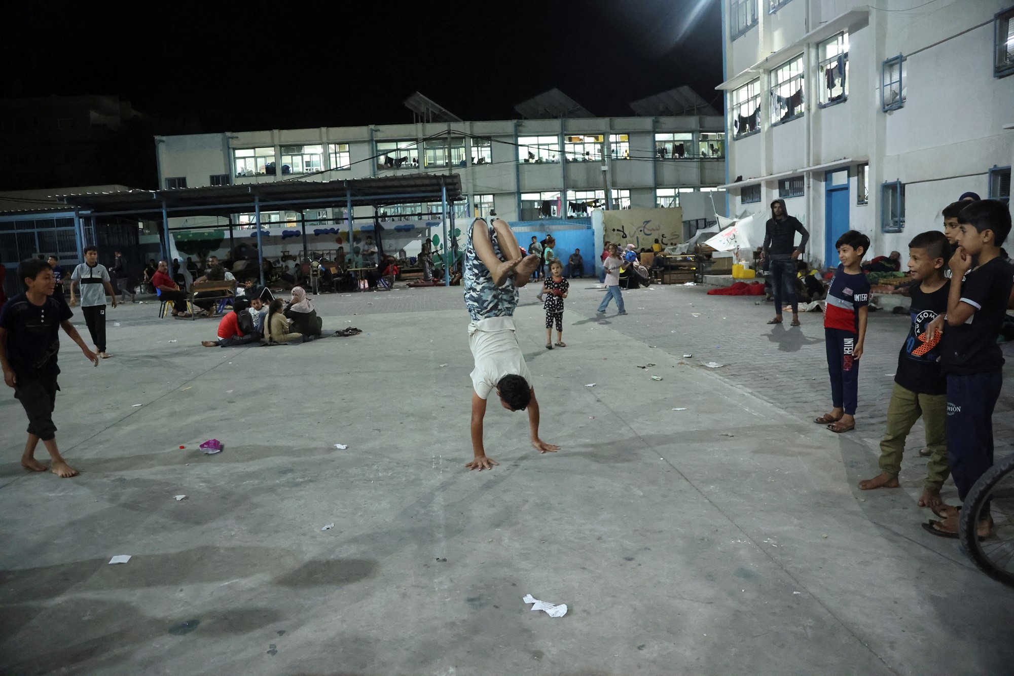 A child does a handstand in a courtyard in front of other children. 