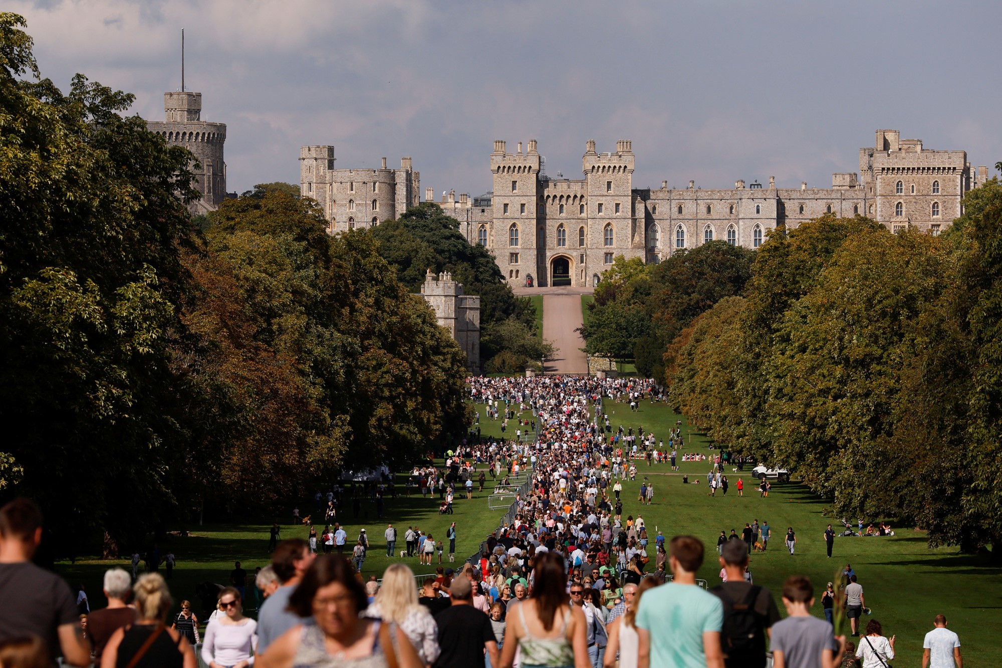 Windsor Castle is pictured, with trees and grass in front of it, where large crowds have gathered.