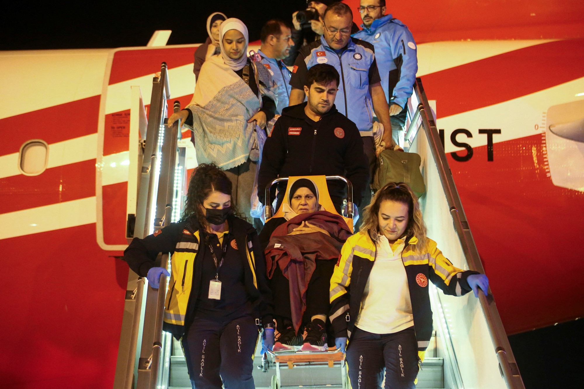 Medical staff carry a woman down plane steps 