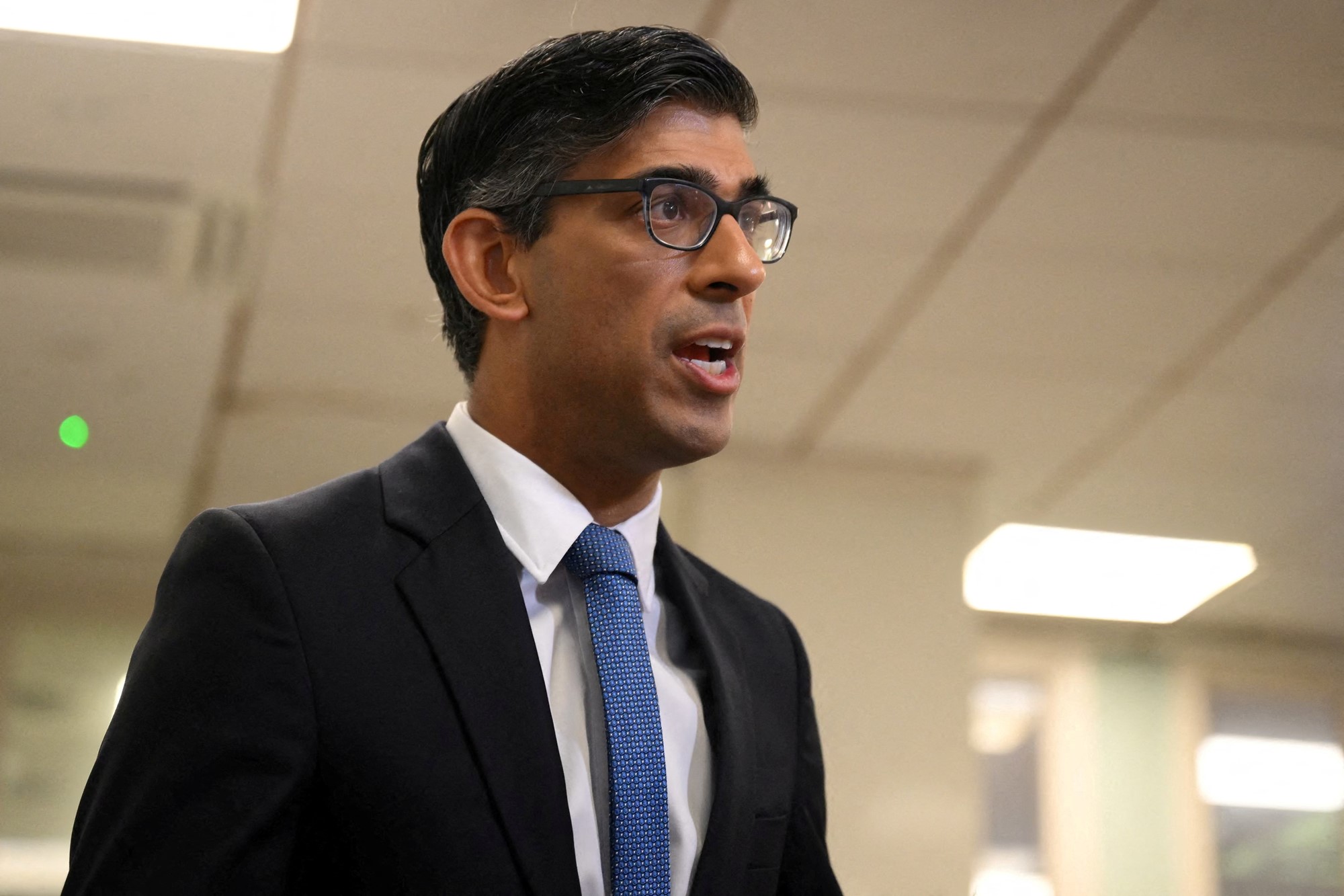 A middle-aged man in a suit and glasses speaks inside an office