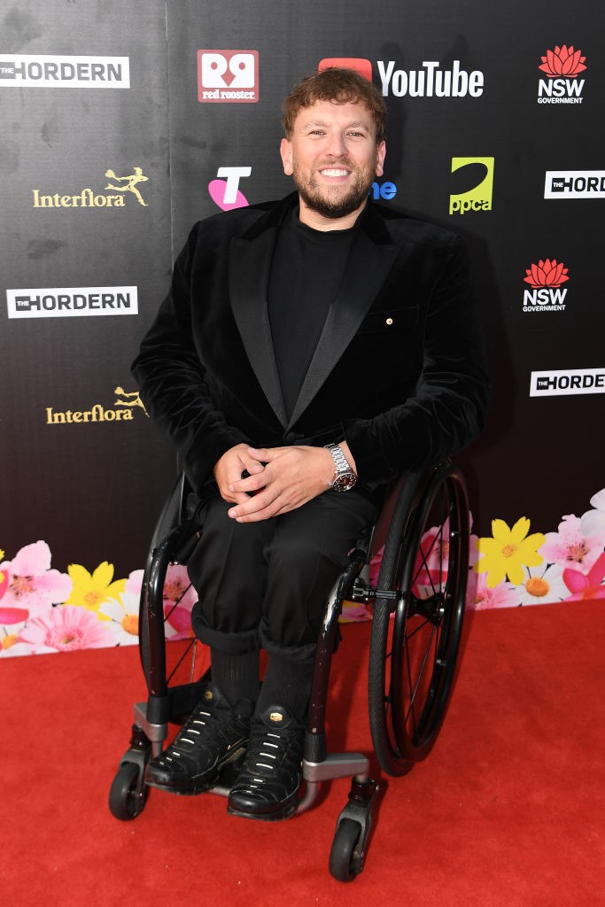 Dylan Alcott poses on the red carpet in a black dress in a wheelchair