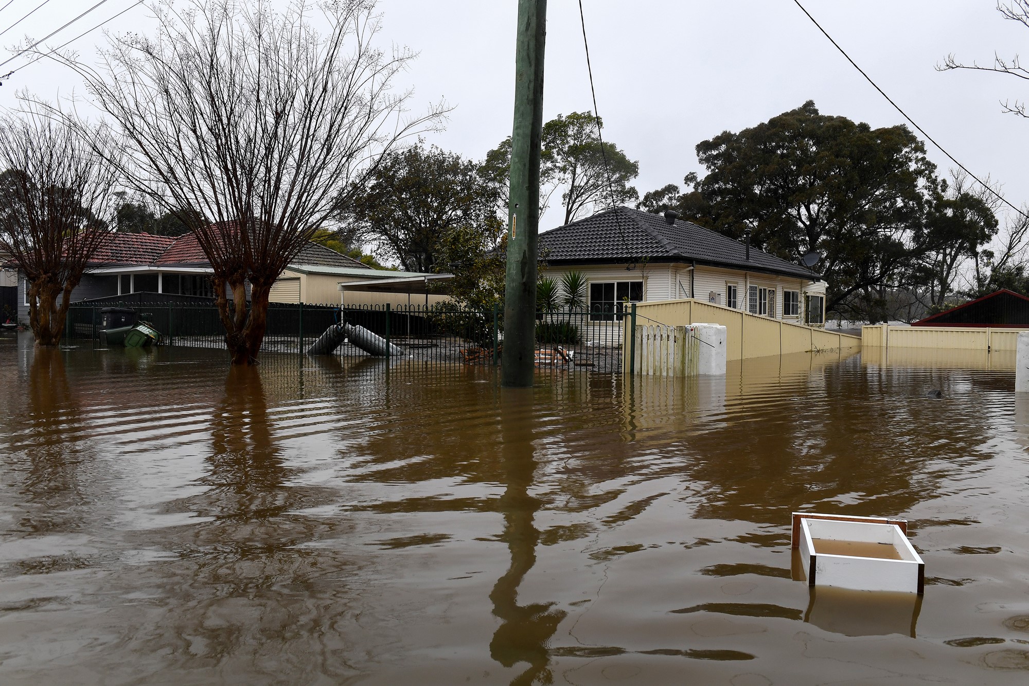 A box floats down a flooded street as homes are seen in the background.