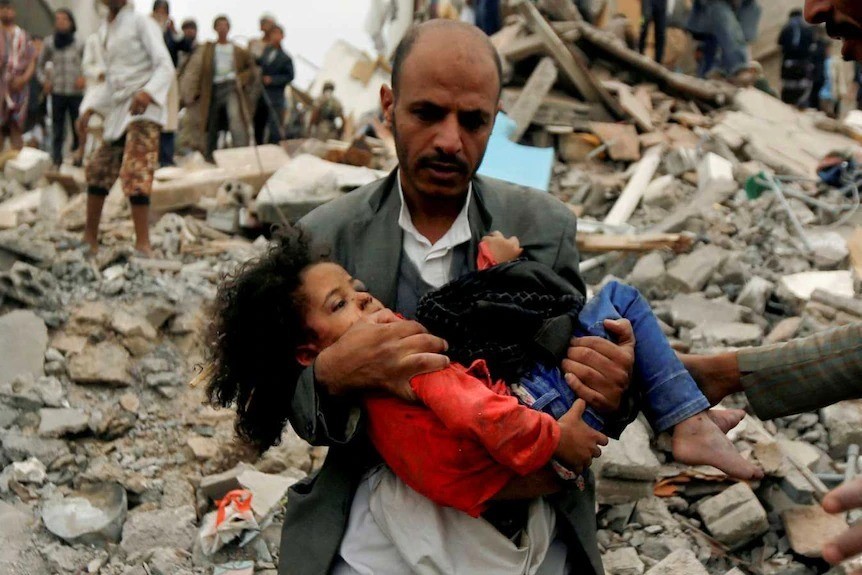Man carries a child from the rubble in Yemen