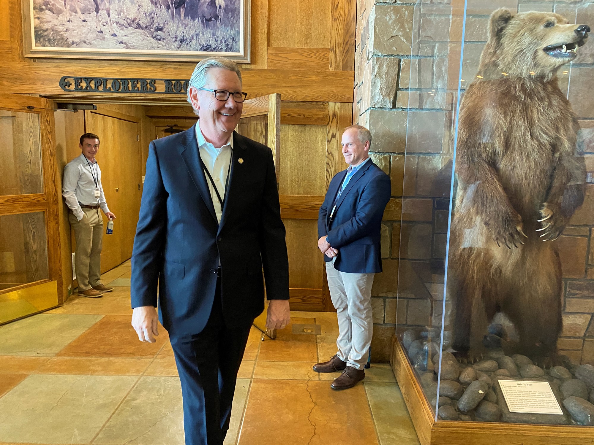 A man walks past a taxidermied grizzly bear in a glass case.