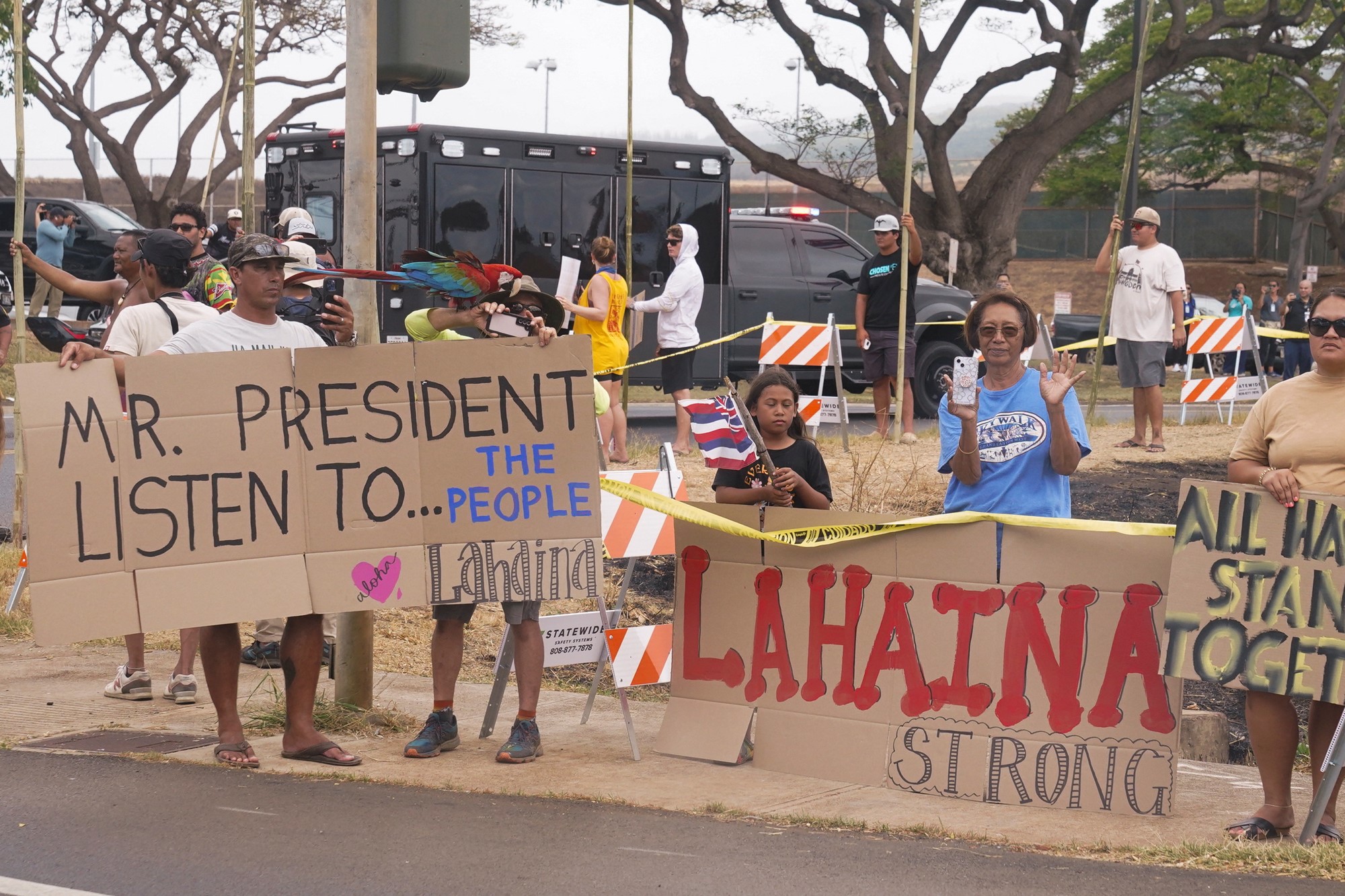 Residents hold up signs that say Lahaina strong and mr president listen to the people 