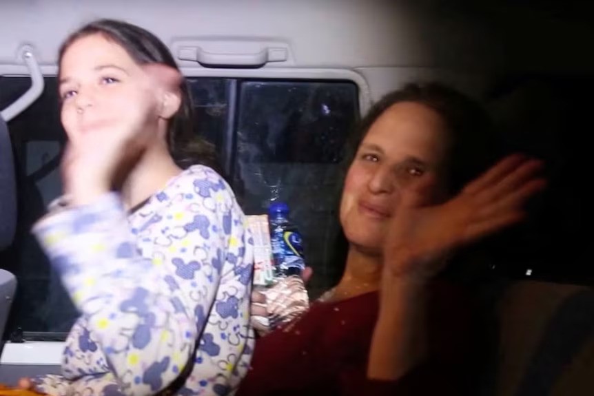 Two female Israeli hostages smiling and waving in a car