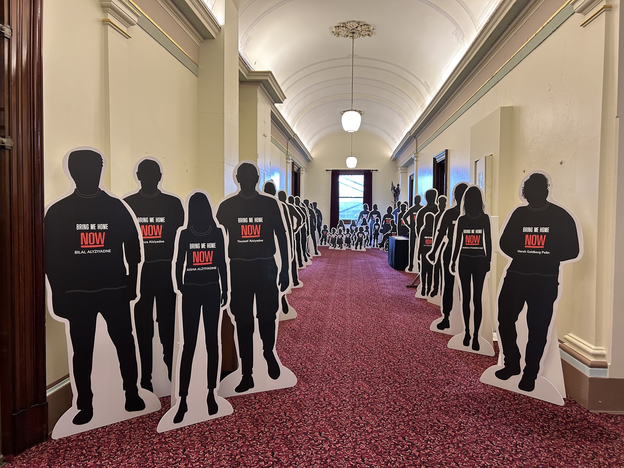 A hallway corridor with red carpet and white walls lines with two dozen silhouette carboard cutouts lined along the side