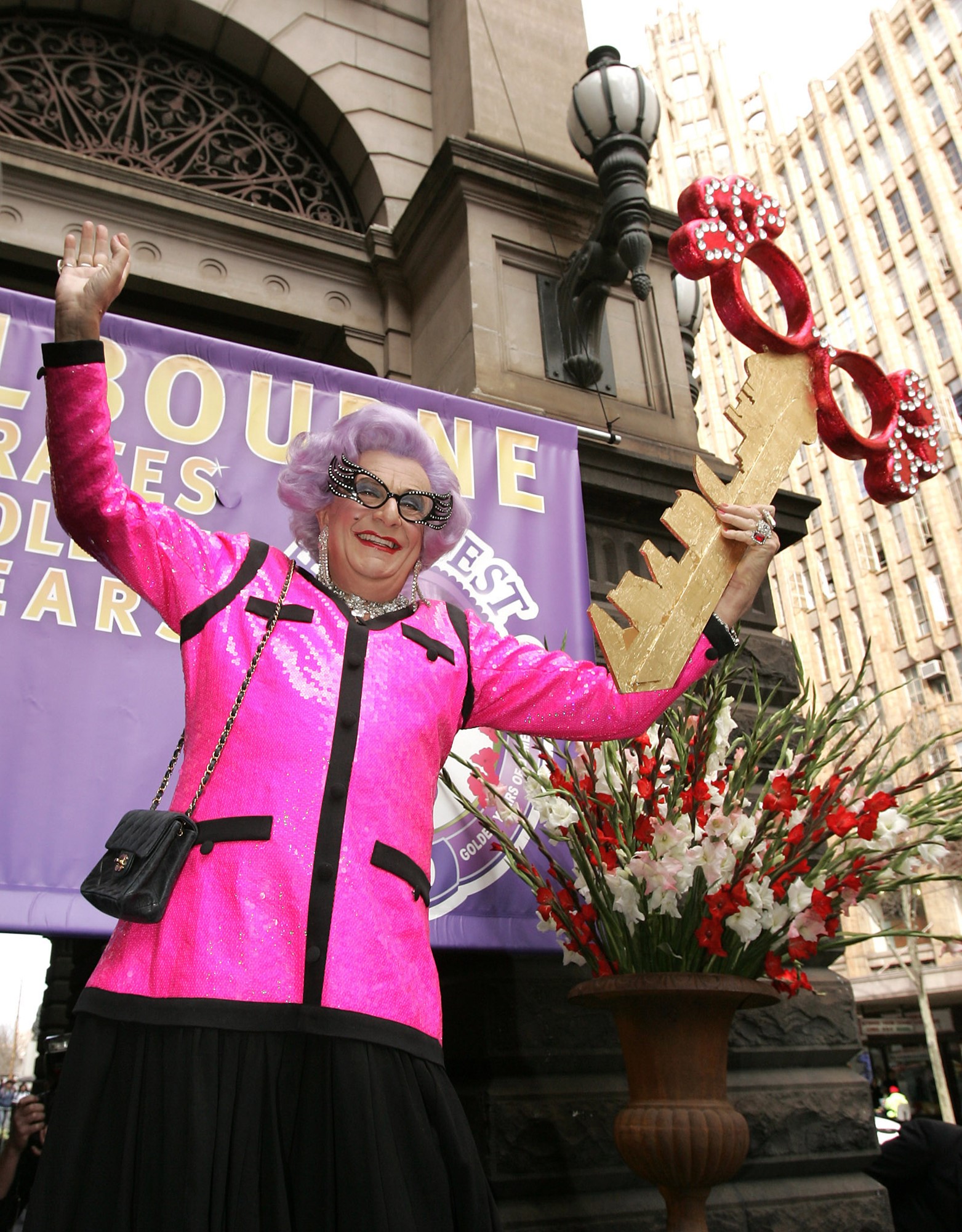 Dame Edna Everage poses holding a large golden key decorated with replica Dame Edna glasses. 