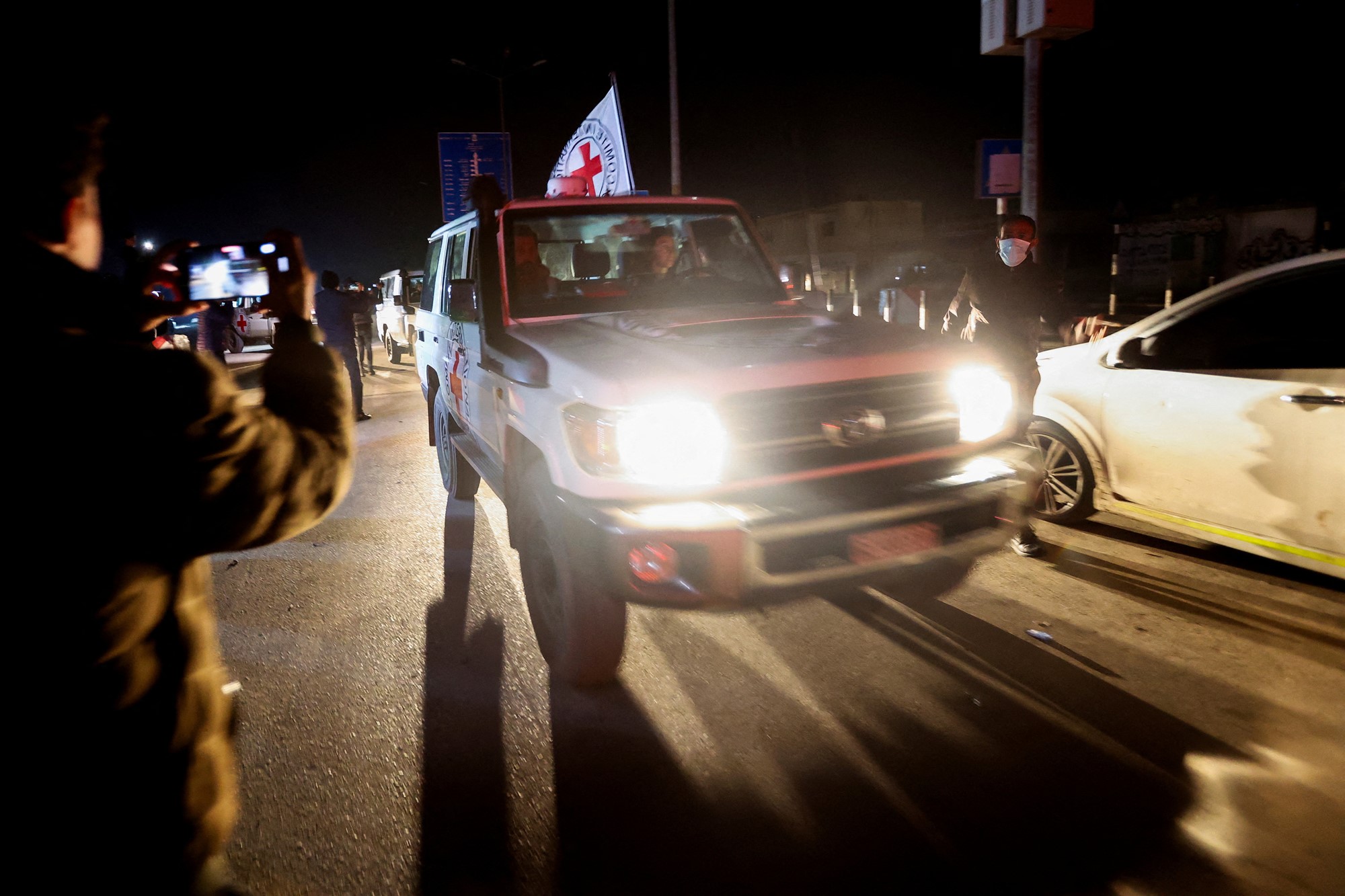 A red cross vehicle drives past photographers