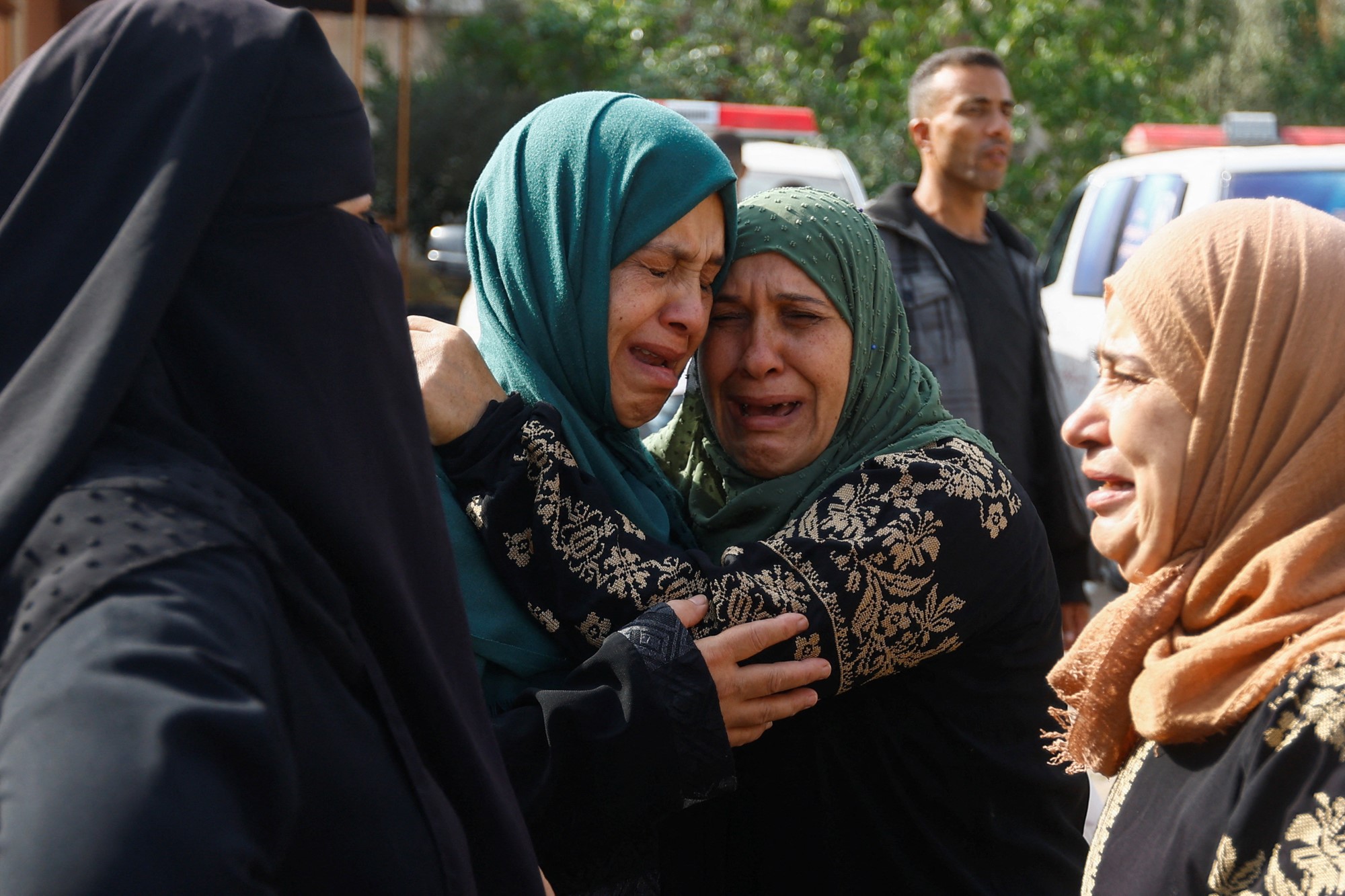 A small group of Palestinian women embrace as they cry.