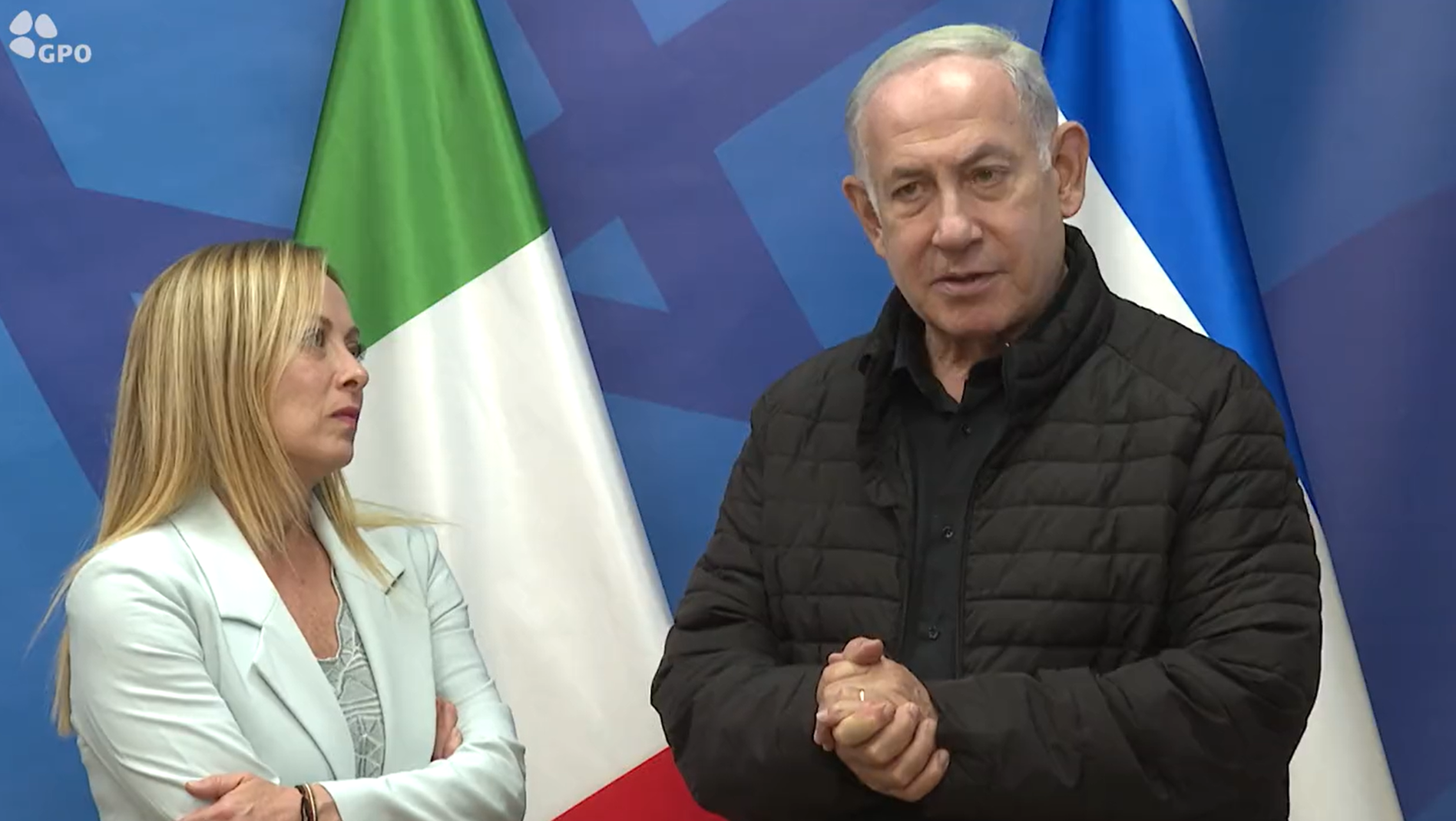 A man in front of an Israeli flag stands next to a woman in front of an Italian flag