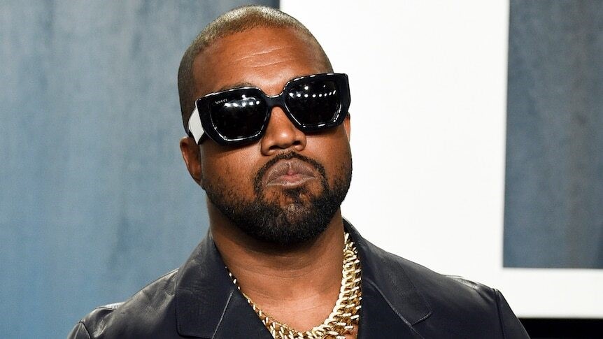 A close up of Kanye at an event in dark sunglasses and a thick gold chain necklace.