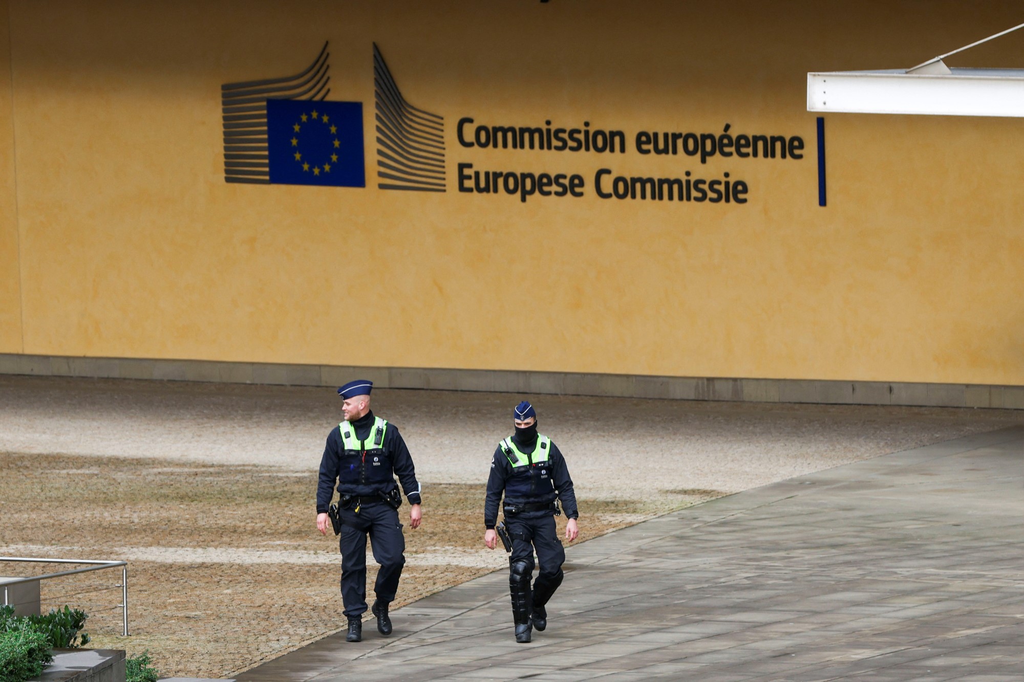Two police walk in front of a building with Europese Commissie written on the front. 
