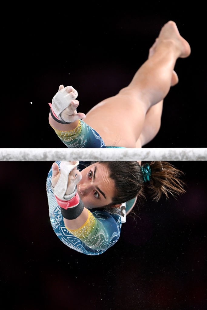 gymnast georgia godwin is captured flying through the air reaching for an uneven bar, her legs are stretched out behind her