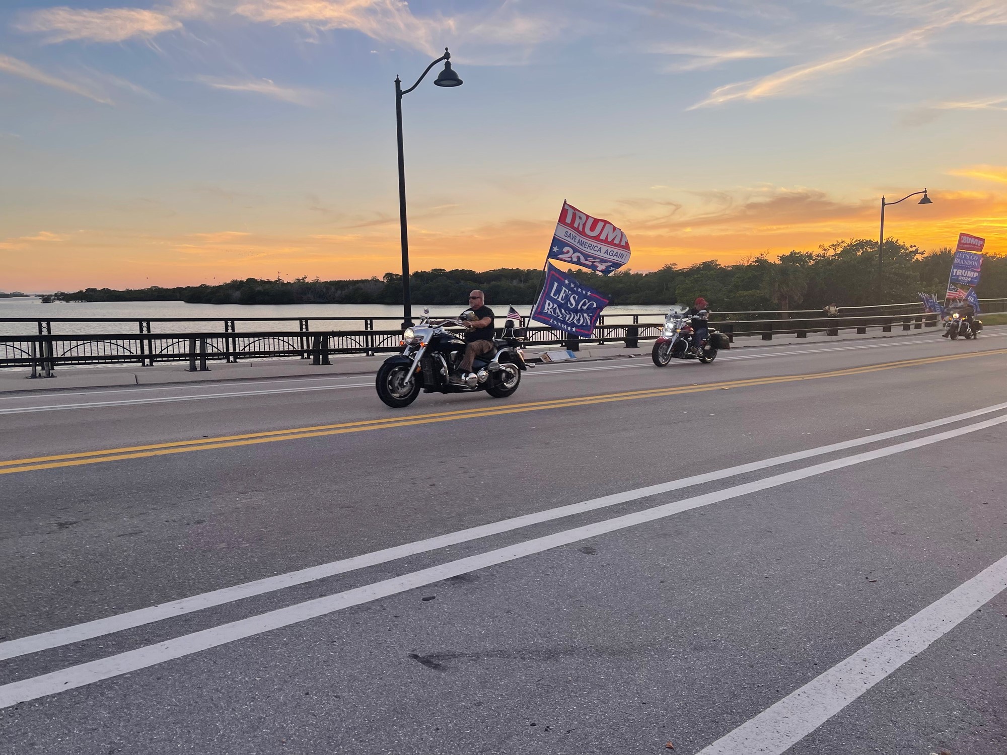 A man drives a motorcycle with a Trump 20224 banner.
