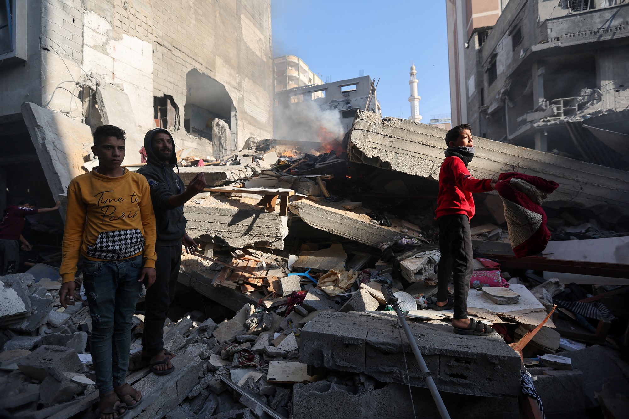 Three children standing amongst rubble with a small fire inside.