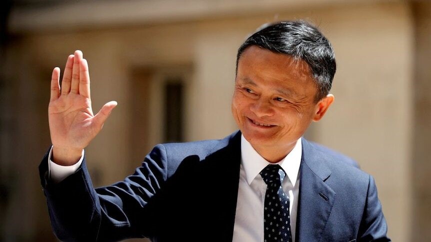 A Chinese man, wearing a business suit, waves at photographers.