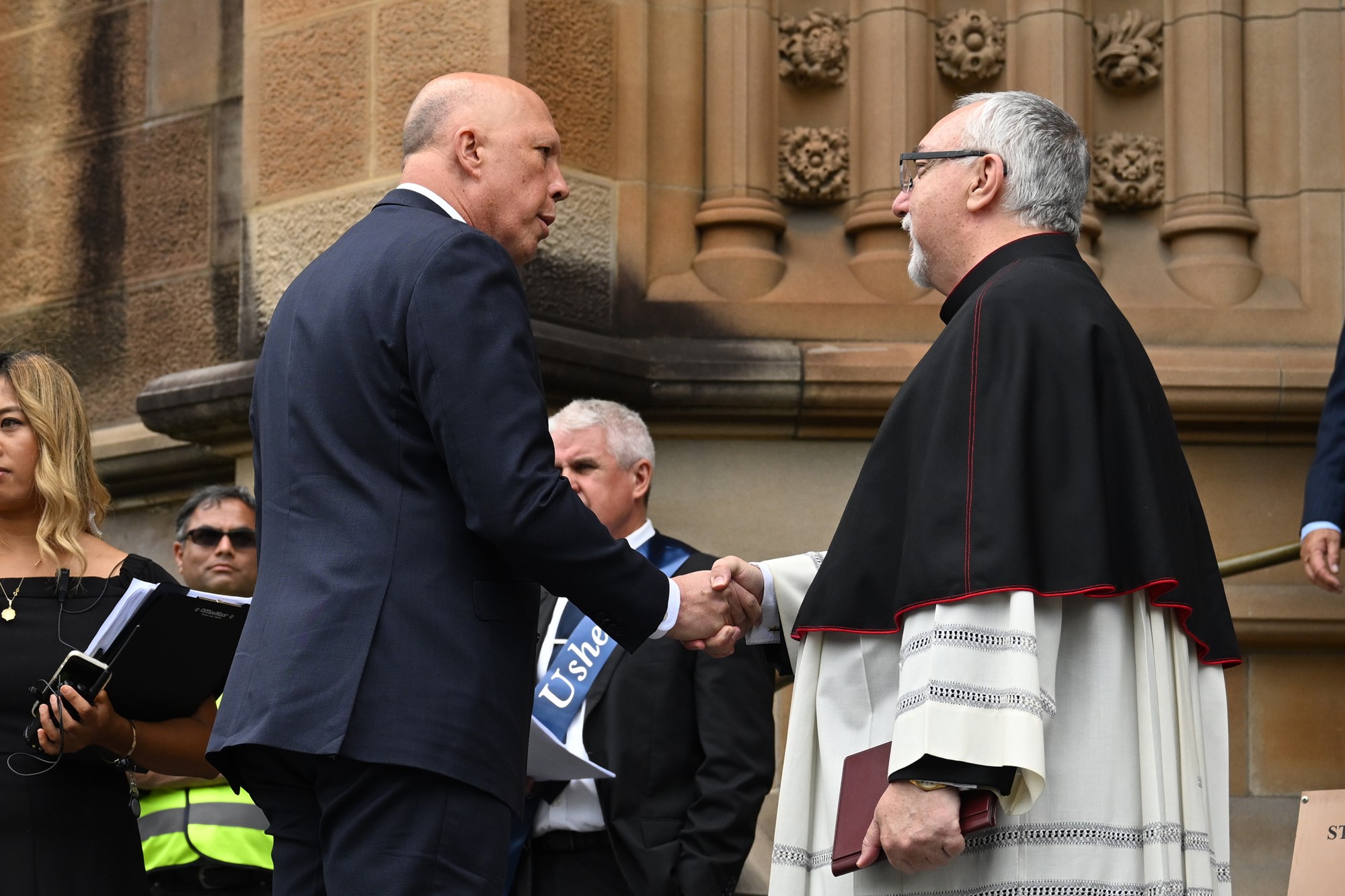 Peter Dutton shakes hands with a man dressed in religious clothing.