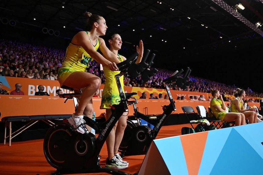 Paige Hadley rides an exercise bike on the sidelines of a Commonwealth Games netball match.