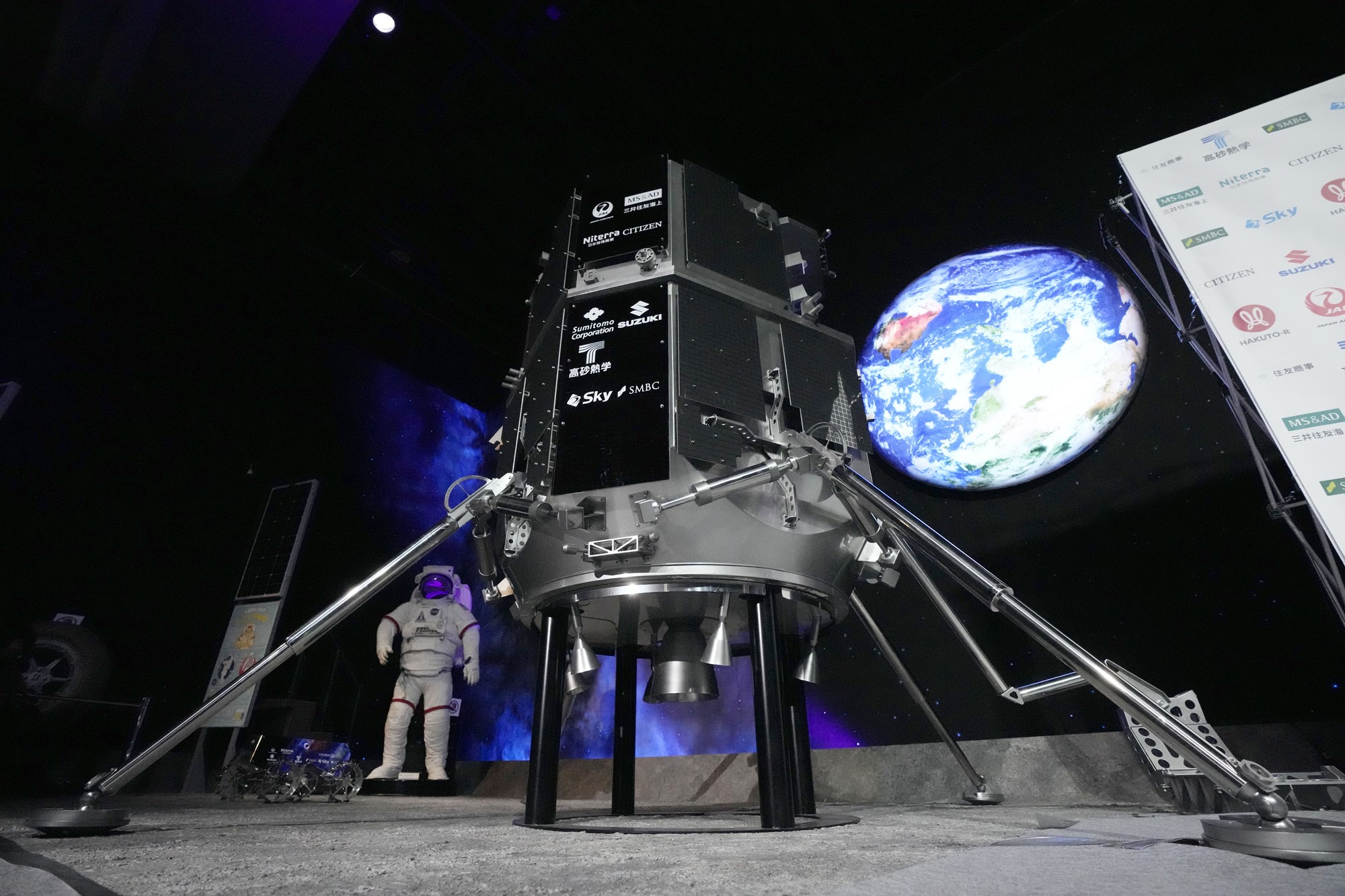 A model lander in front of a screen that shows planet Earth above it.