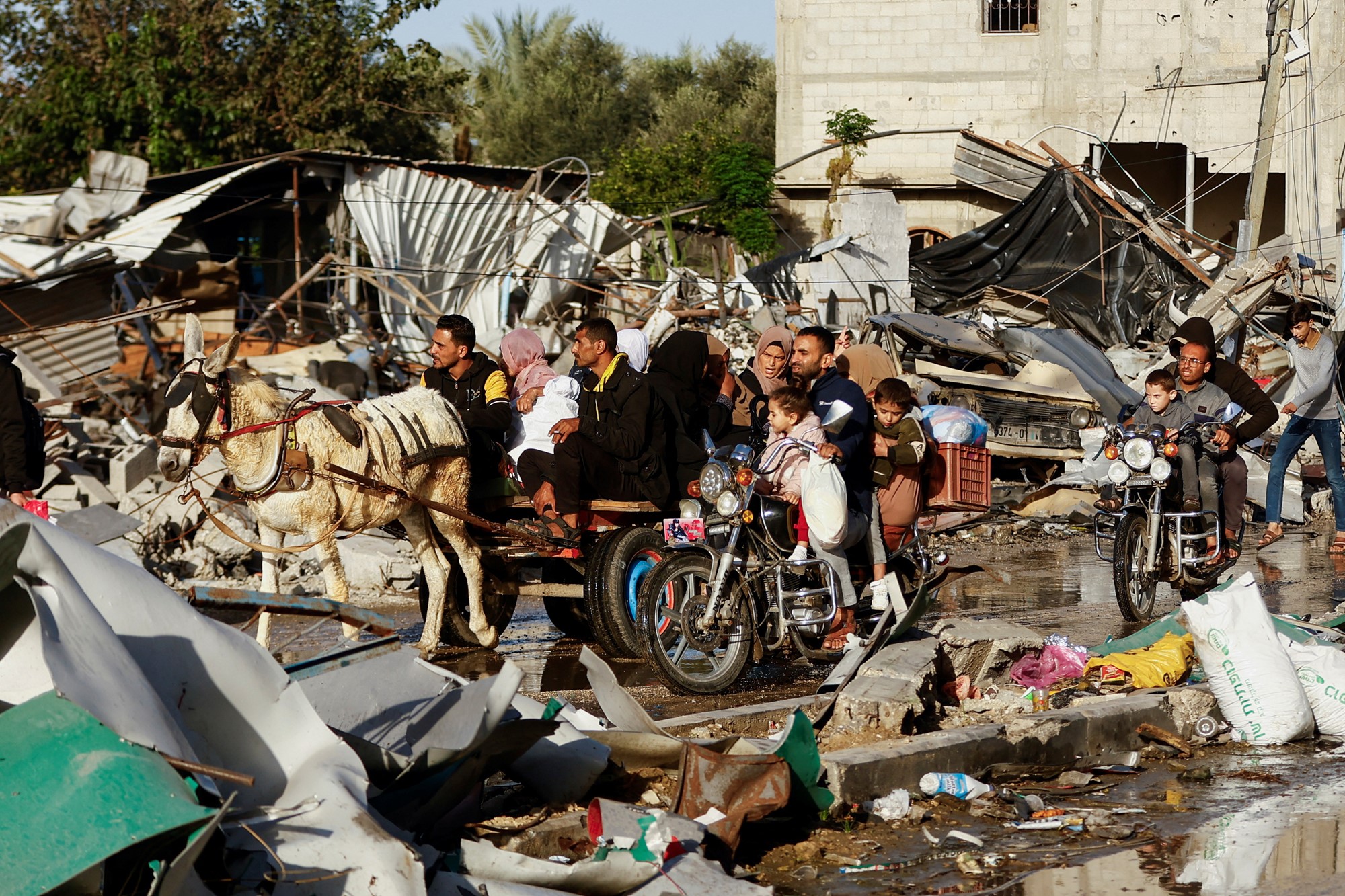A group of people sits on a donkey cart as it moves through an area with destroyed buildings.