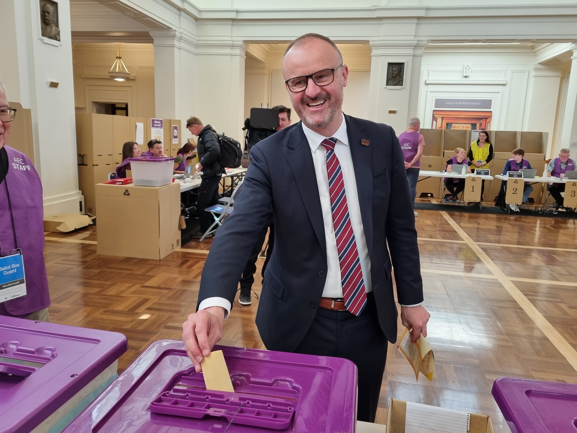 Andrew smiles for a photo as he drops his vote into a purple ballot box.