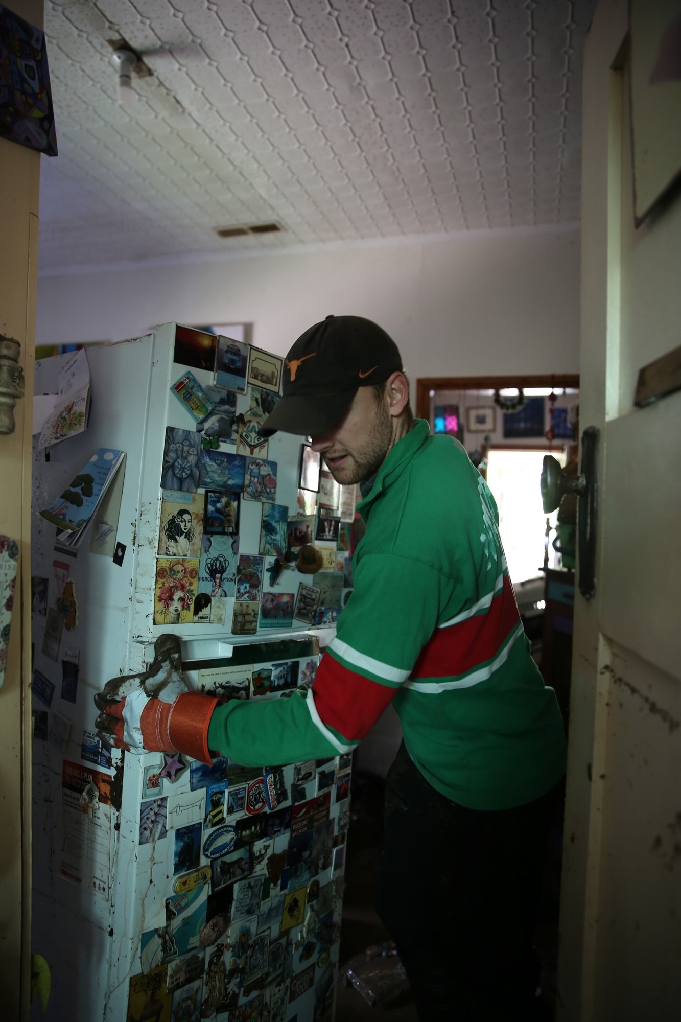 A man wearing gloves and a cap moves a fridge.