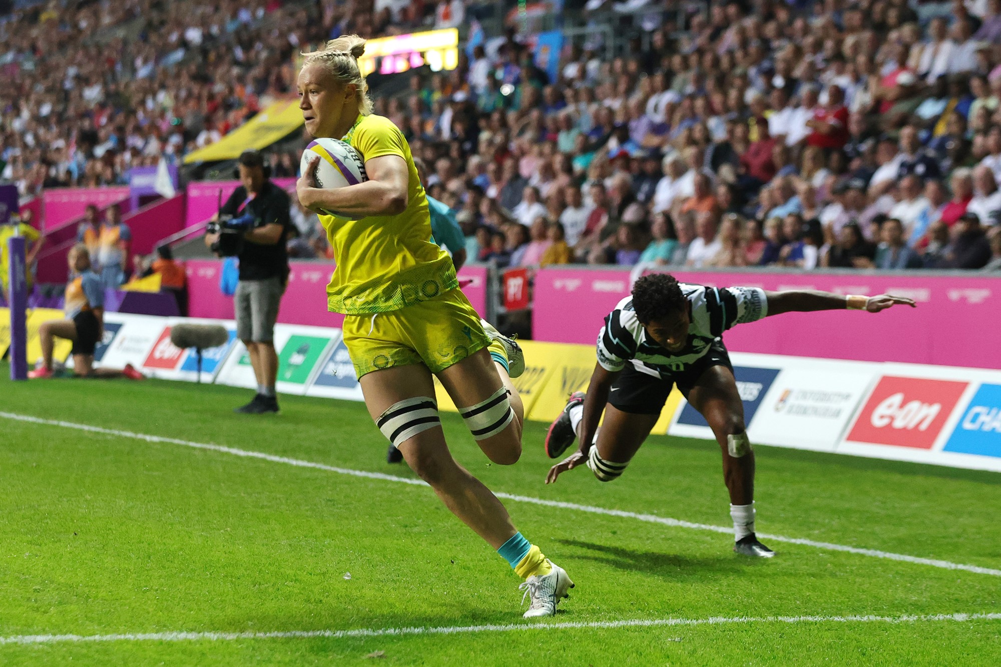 An Australian rugby sevens player runs round to score a try, as her Fijian opponent is left off-balance, behind her.