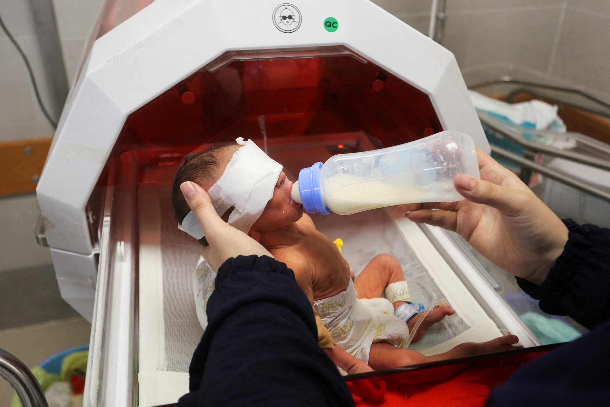 Person hold up premature baby's head and feed it with a bottle 