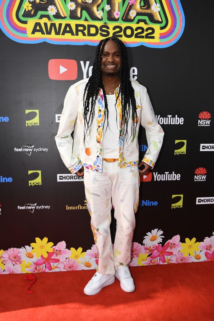 baker boy poses on red carpet wearing white pants and jacket