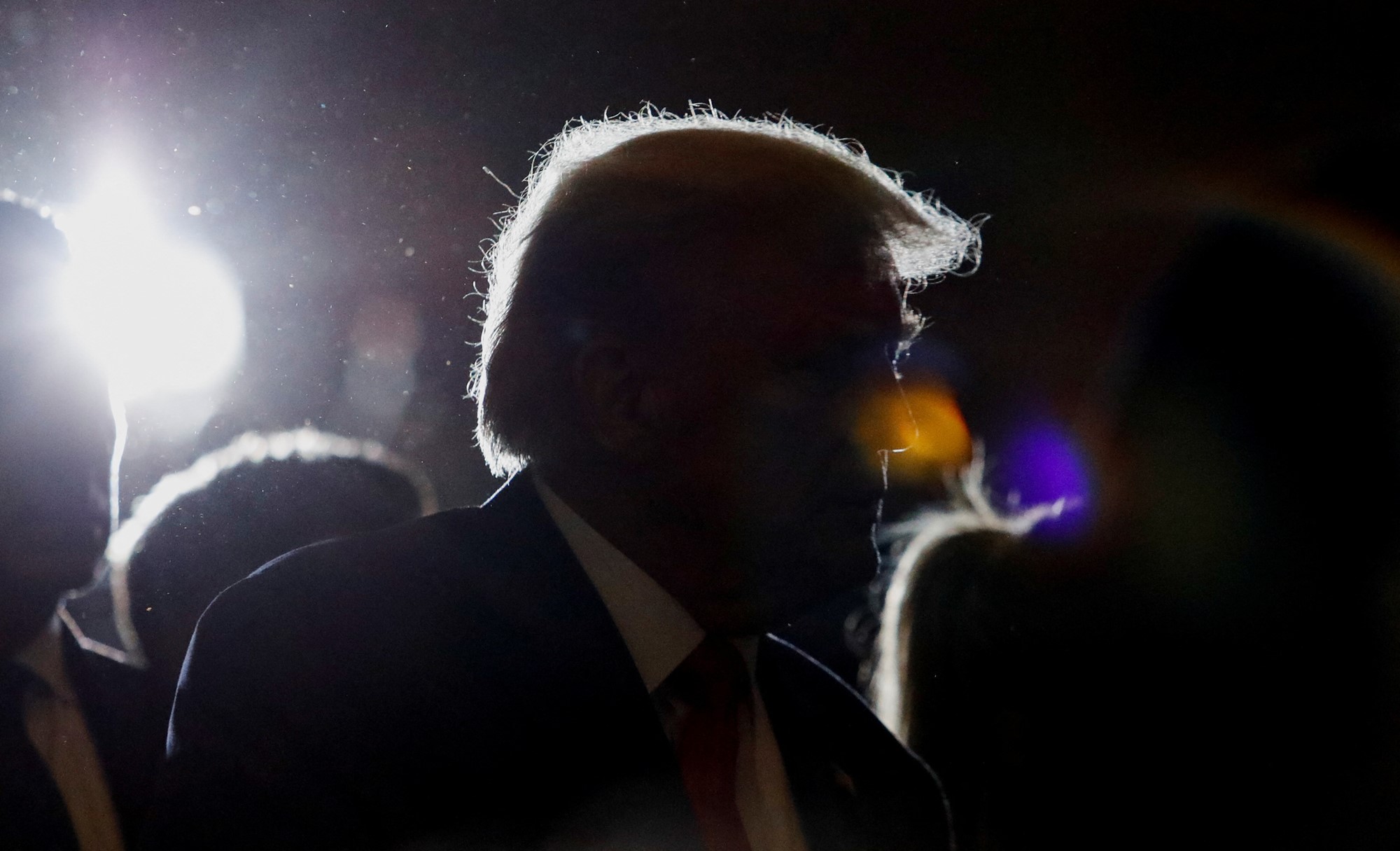 A dark image of Trump where camera flashes show only his silhouette.