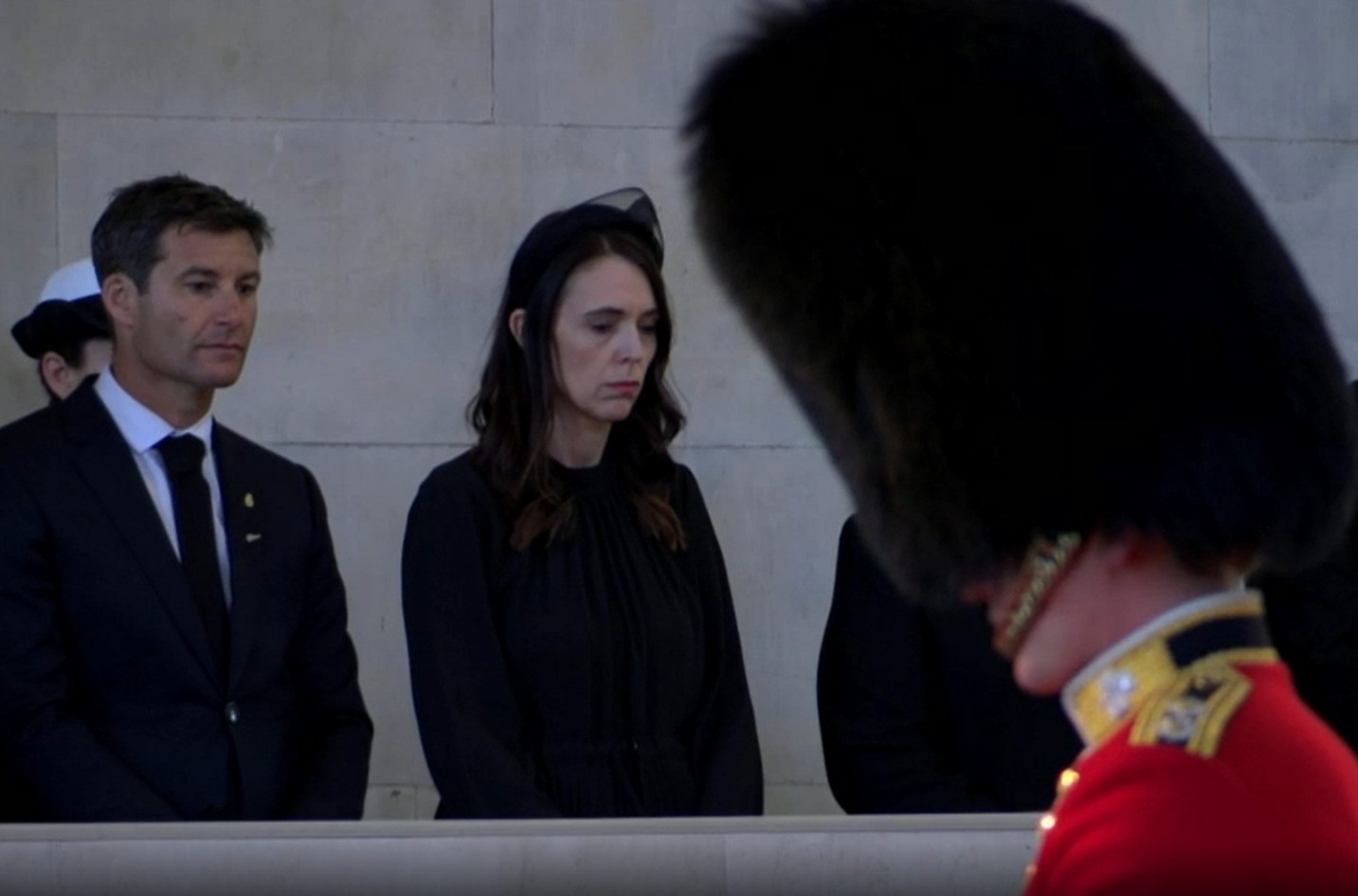 A woman stressed in all black stands solemnly.