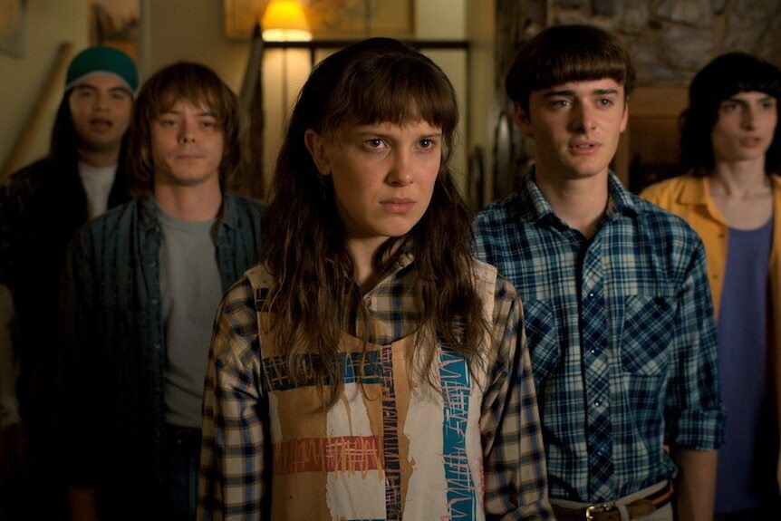 A screengrab of Stranger Things with Eleven standing at the front of the group, with Will by her side.